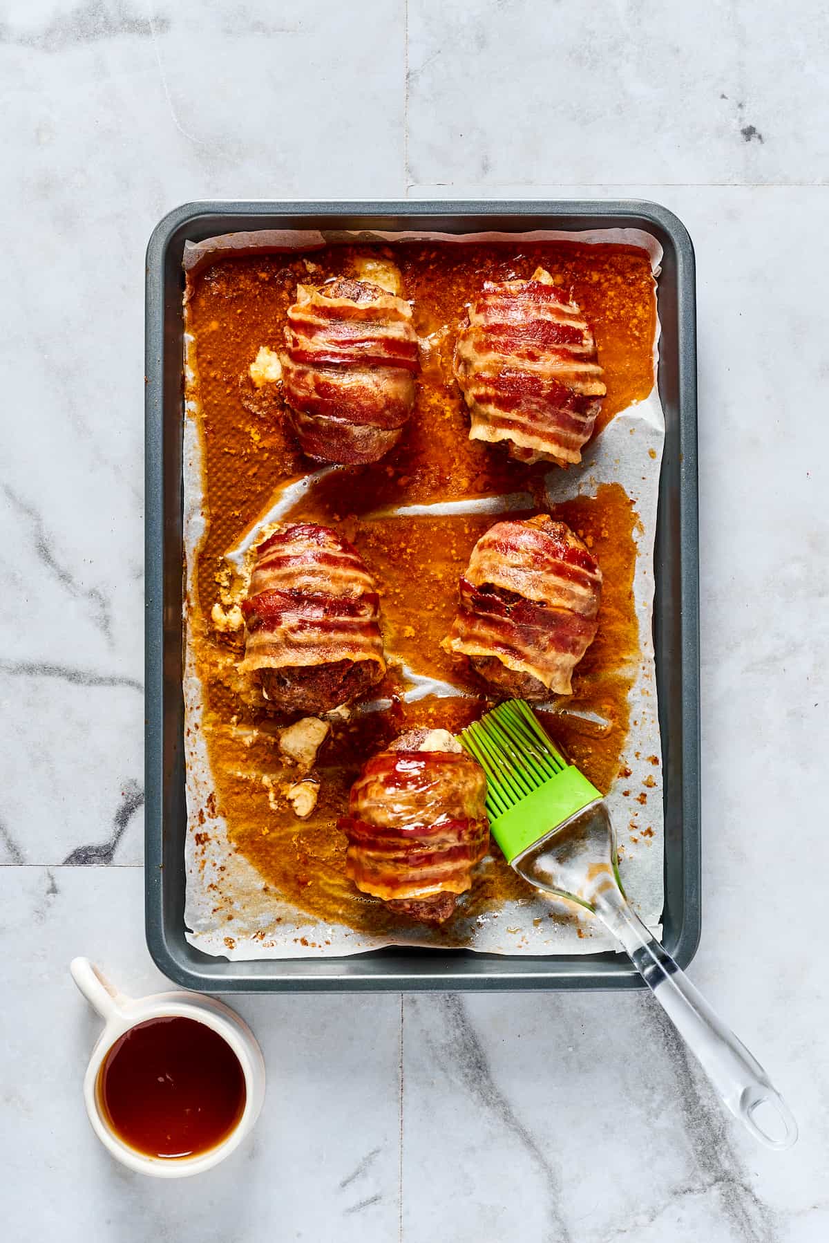 If you love jalapeno poppers, you are going to LOVE these Armadillo Eggs - cheese-stuffed jalapenos wrapped in bacon and sausage. Yum! BBQ sauce being spread over armadillo eggs