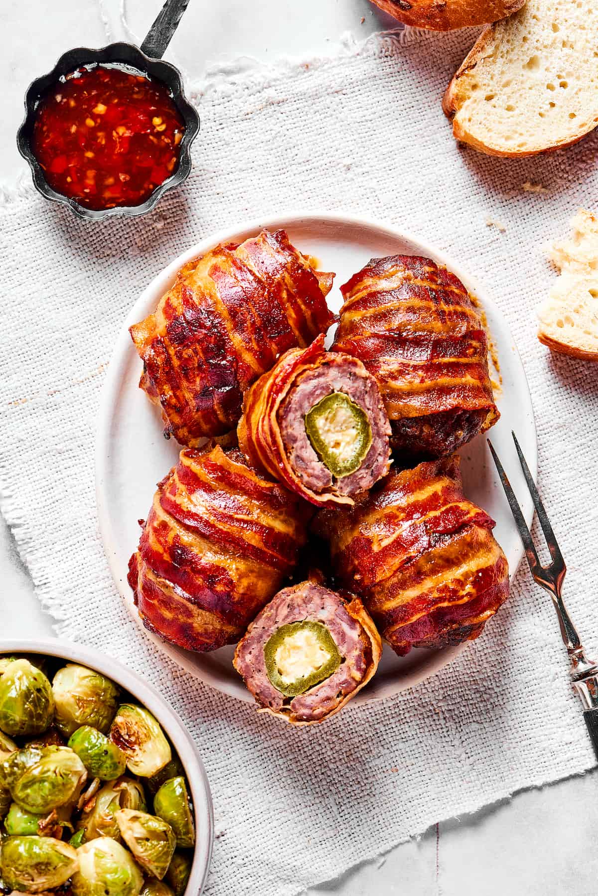 If you love jalapeno poppers, you are going to LOVE these Armadillo Eggs - cheese-stuffed jalapenos wrapped in bacon and sausage. Yum! Overhead view of bacon wrapped armadillo eggs on a plate, with one cut in half
