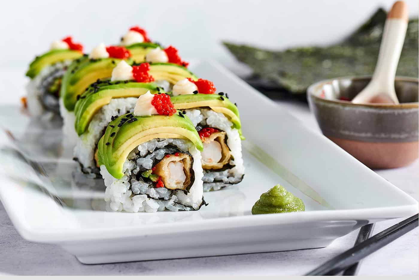This dragon roll features tempura shrimp, cucumber, tobiko, and avocado wrapped in nori and rice. It's easy to make and such a crowd-pleaser! A sushi roll with shrimp tempura and avocado.