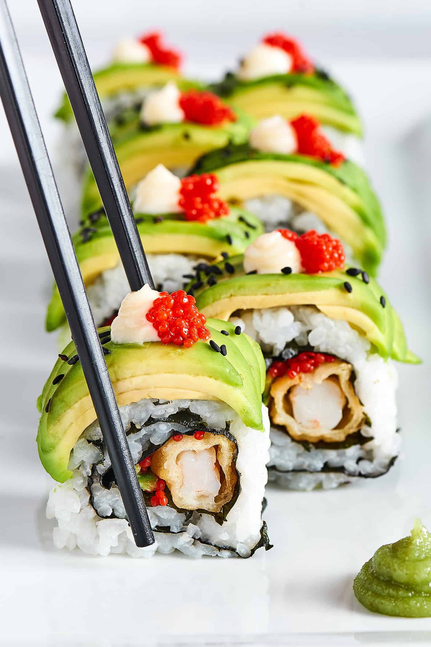 This dragon roll features tempura shrimp, cucumber, tobiko, and avocado wrapped in nori and rice. It's easy to make and such a crowd-pleaser! Chopsticks picking up a piece of sushi roll.