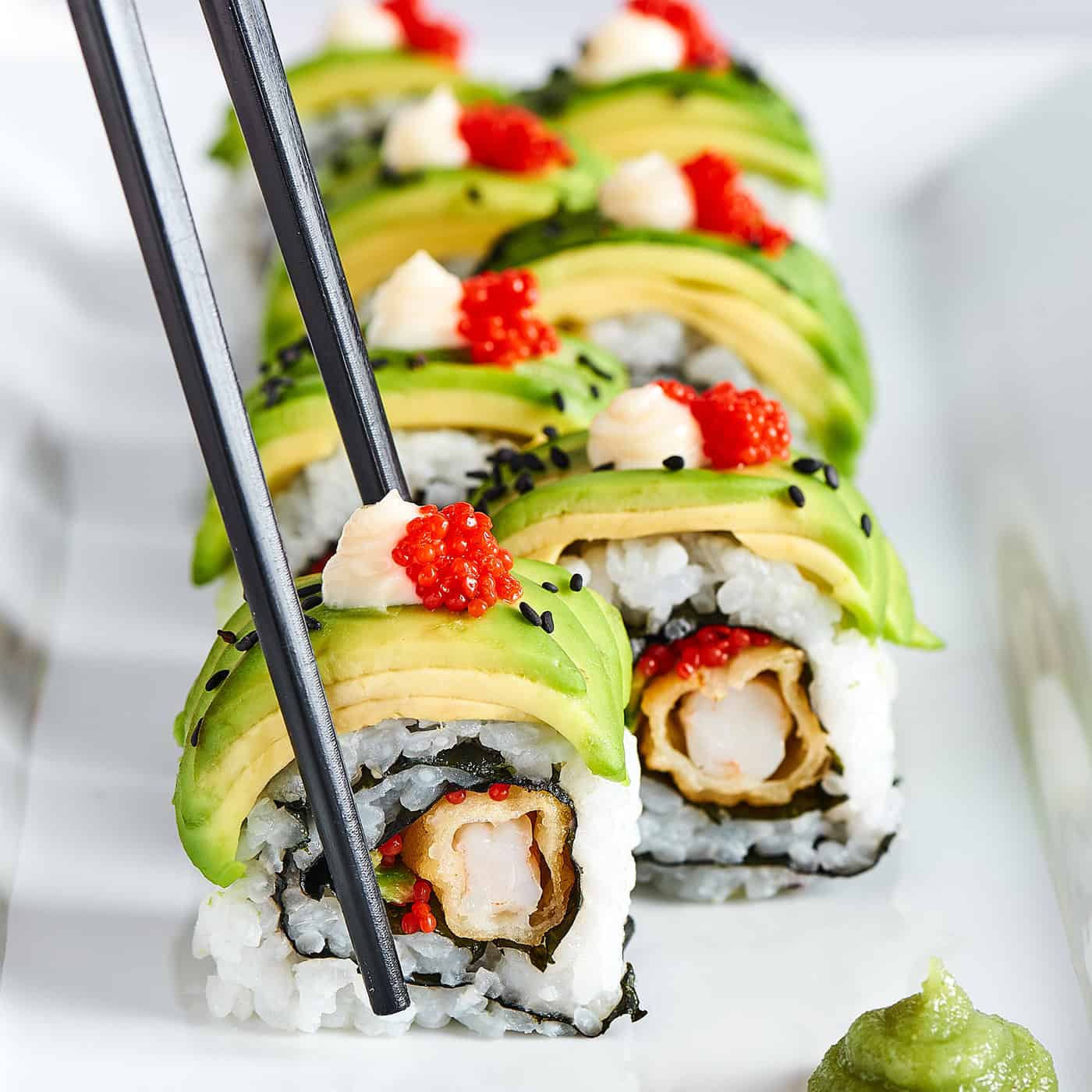 This dragon roll features tempura shrimp, cucumber, tobiko, and avocado wrapped in nori and rice. It's easy to make and such a crowd-pleaser! Chopsticks picking up a piece of sushi roll.