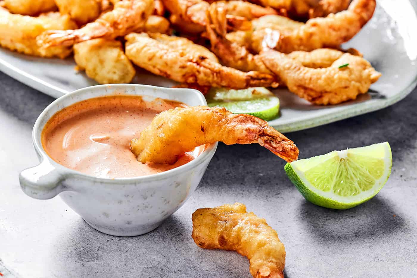 This easy shrimp tempura recipe features juicy, tender shrimp dipped in a light tempura batter. It's then deep-fried until perfectly crispy! dipping shrimp tempura into a small bowl of creamy sauce