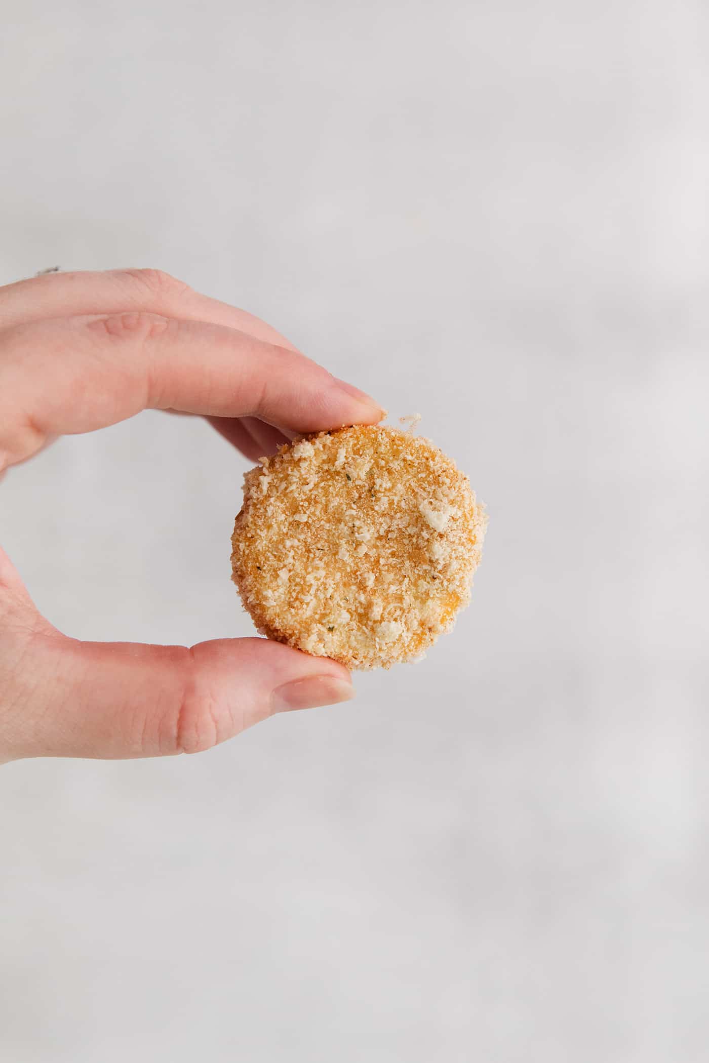 This easy, flavorful fried yellow squash is delightfully crispy on the outside and tender on the inside. Grab your favorite dip and enjoy! A hand holding a squash rounded coated in bread crumbs
