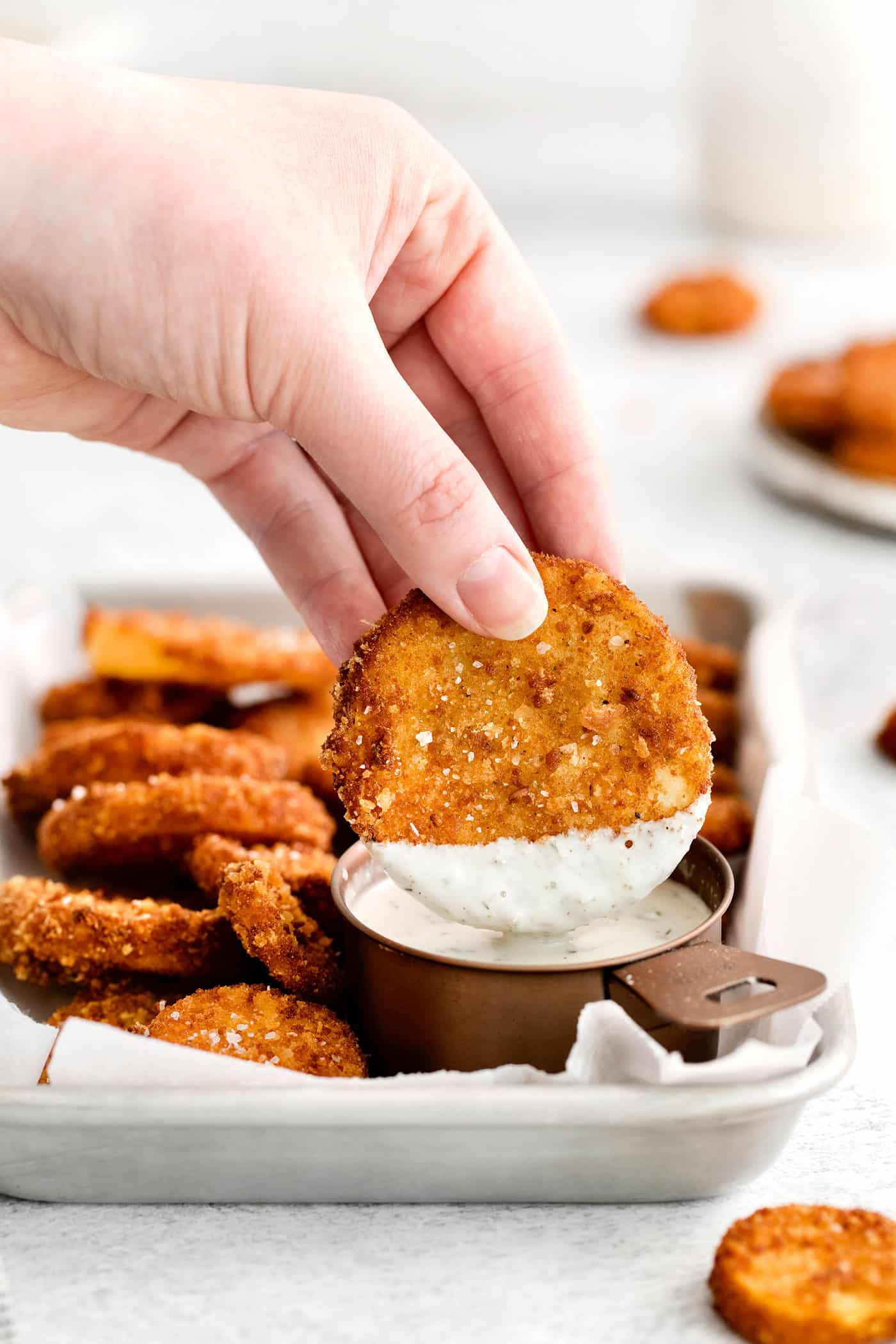 This easy, flavorful fried yellow squash is delightfully crispy on the outside and tender on the inside. Grab your favorite dip and enjoy! A hand holding a squash round dipped into ranch