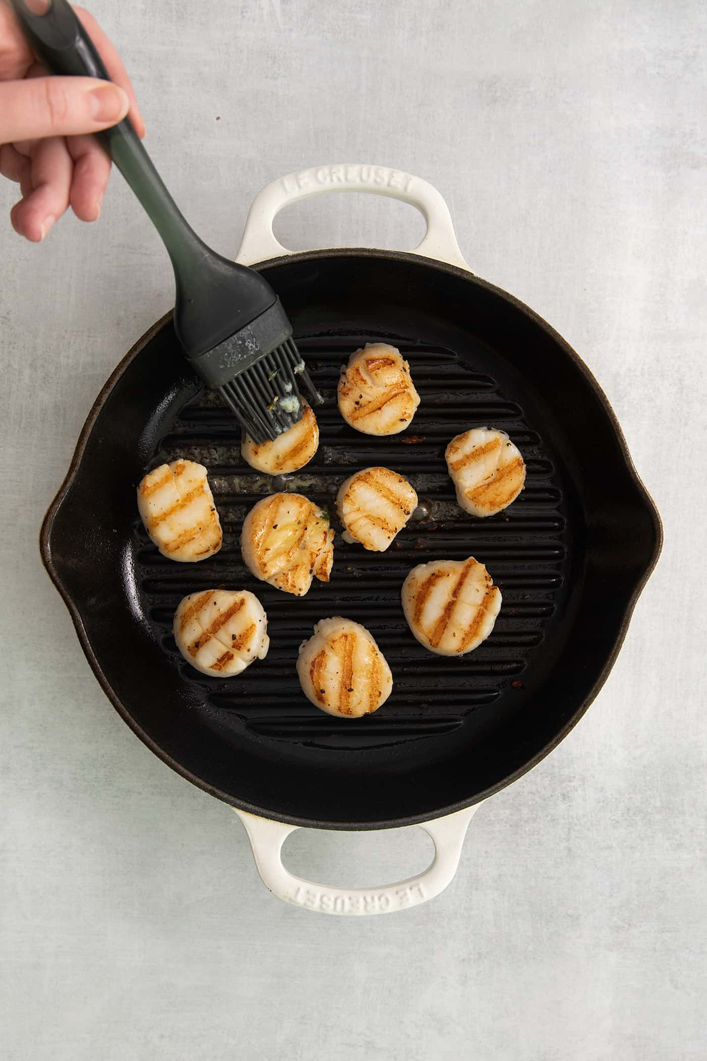 These easy grilled sea scallops are done in 20 minutes and richly flavored with garlic butter and lemon. Cook on an indoor or outdoor grill! Garlic butter being brushed on grilled scallops