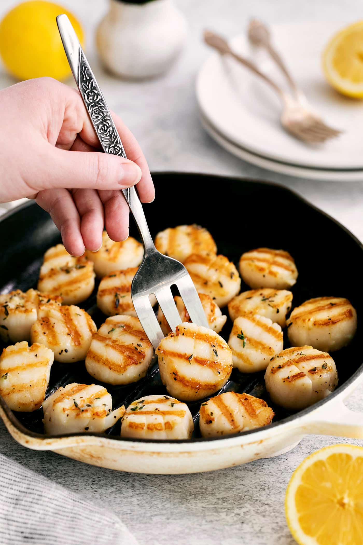 These easy grilled sea scallops are done in 20 minutes and richly flavored with garlic butter and lemon. Cook on an indoor or outdoor grill! A fork turning up a scallop in a grill pan