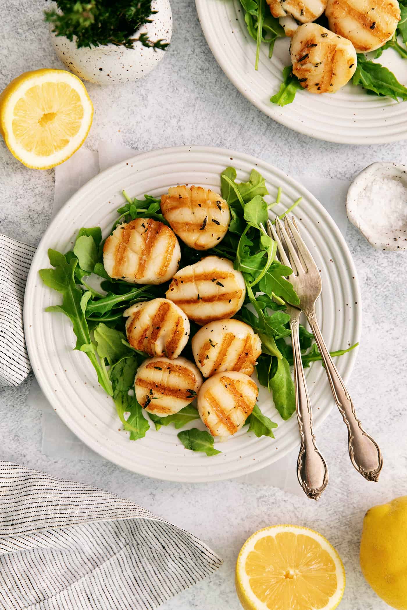 These easy grilled sea scallops are done in 20 minutes and richly flavored with garlic butter and lemon. Cook on an indoor or outdoor grill! Grilled scallops on a bed of greens