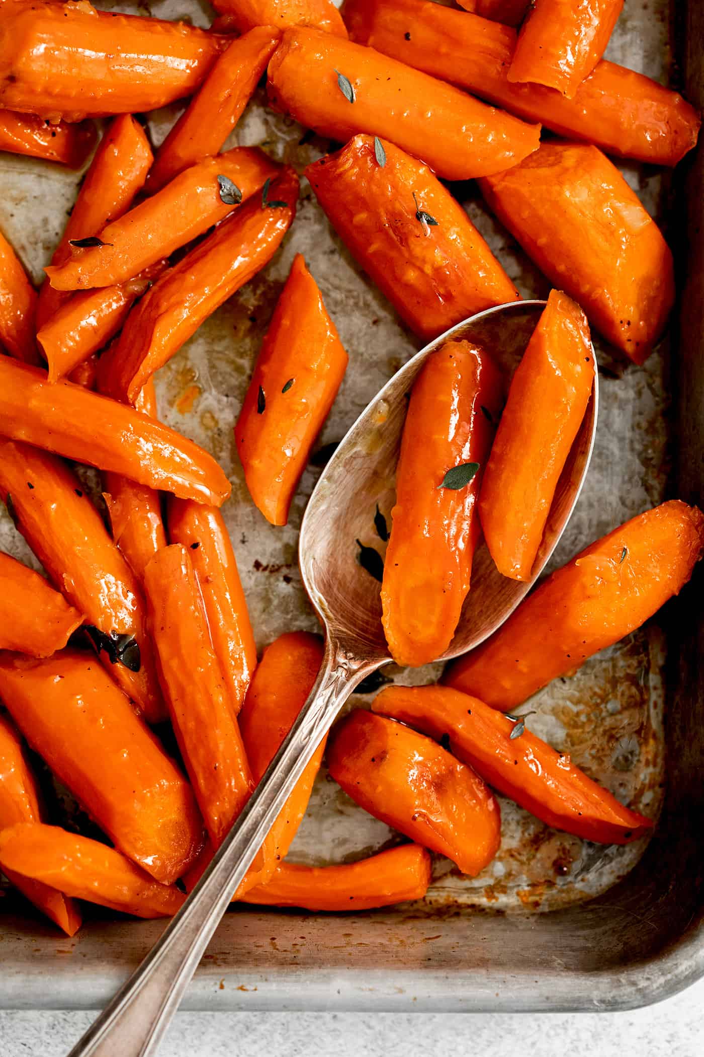 A spoon with some honey garlic roasted carrots over a baking sheet