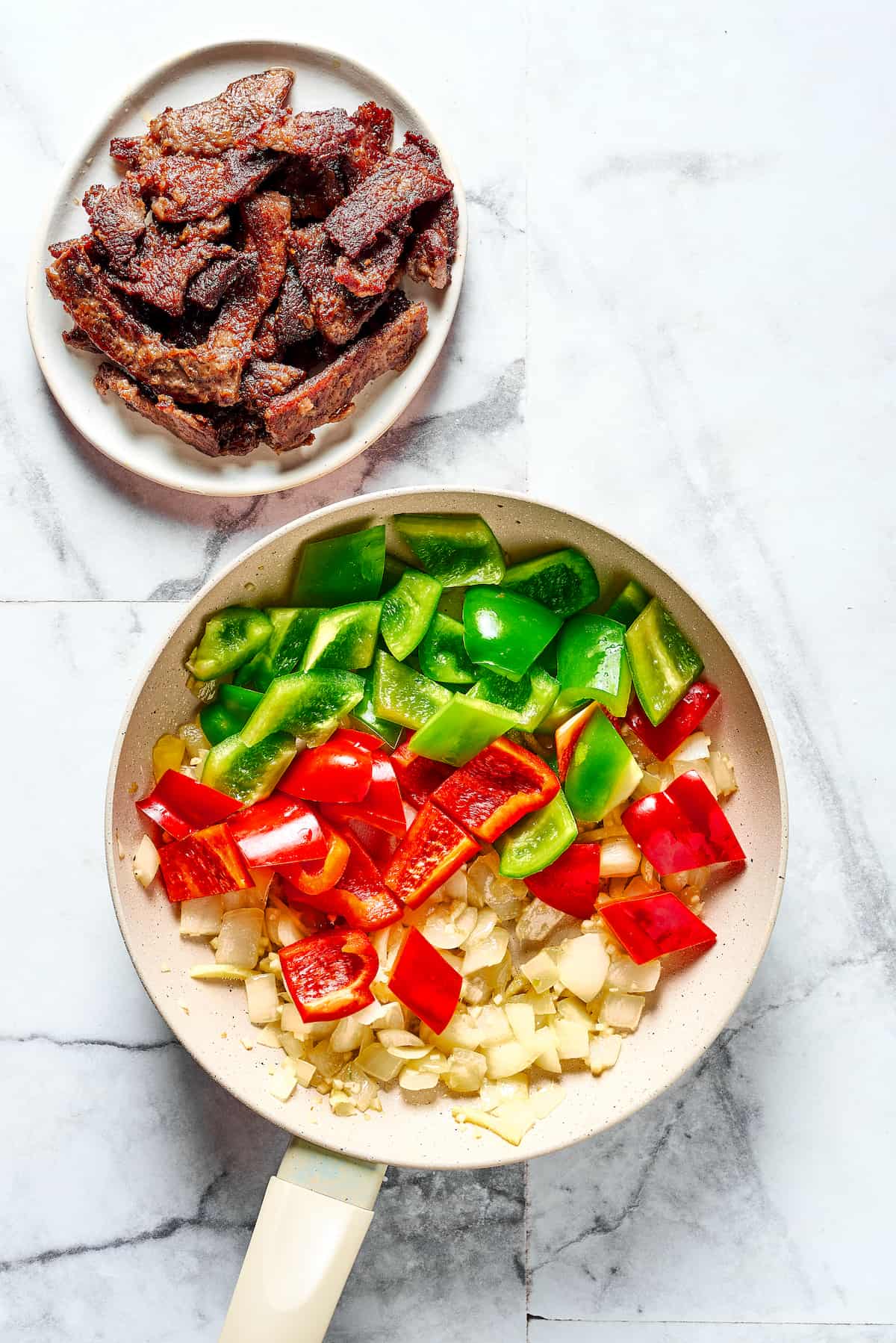 This Easy Hunan Beef recipe is better than take-out! Made with strips of steak, peppers, and onions in a savory, mildly hot, and tangy sauce. Onions and bell peppers in a skillet