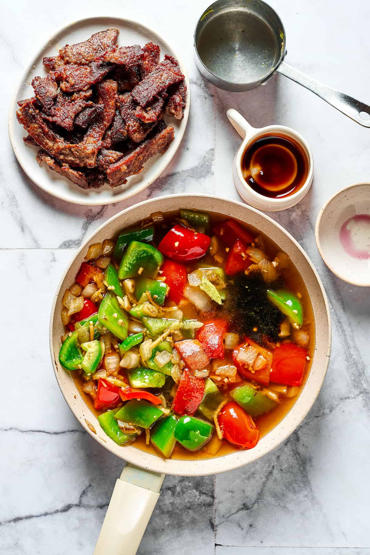 This Easy Hunan Beef recipe is better than take-out! Made with strips of steak, peppers, and onions in a savory, mildly hot, and tangy sauce. Cooked peppers and onions in a skillet