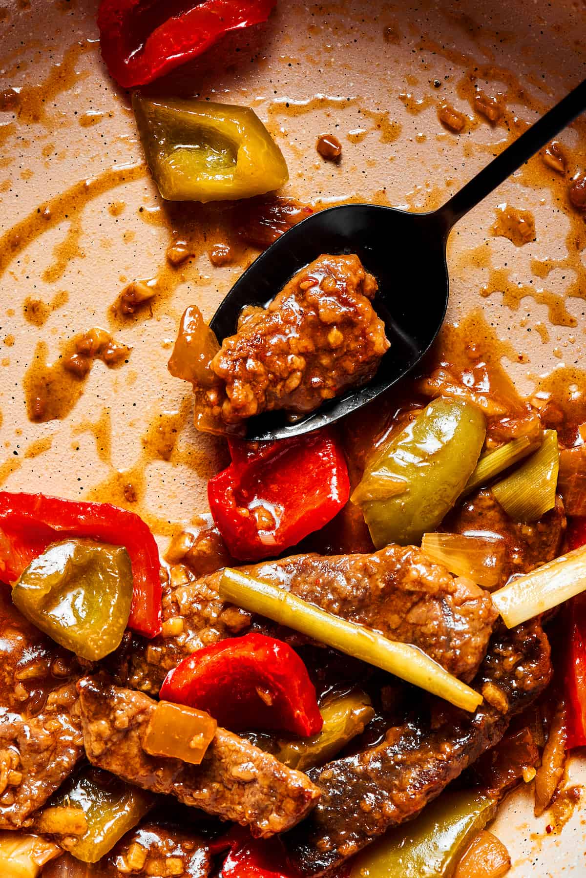 This Easy Hunan Beef recipe is better than take-out! Made with strips of steak, peppers, and onions in a savory, mildly hot, and tangy sauce. A black spoon stirring beef stir fry