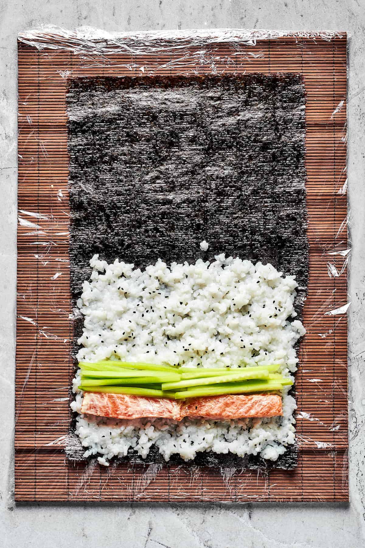 This Sushi Burrito recipe results in a giant sushi roll stuffed with spicy salmon, rice, avocado, carrots, and other veggies. Rice, salmon, and avocado on nori sheets