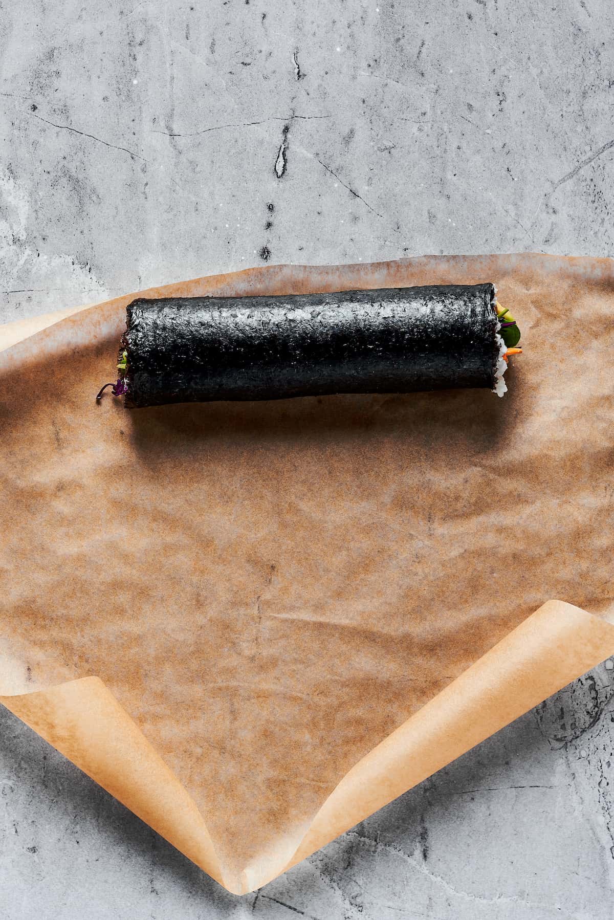 This Sushi Burrito recipe results in a giant sushi roll stuffed with spicy salmon, rice, avocado, carrots, and other veggies. Overhead view of a sushi burrito on brown paper