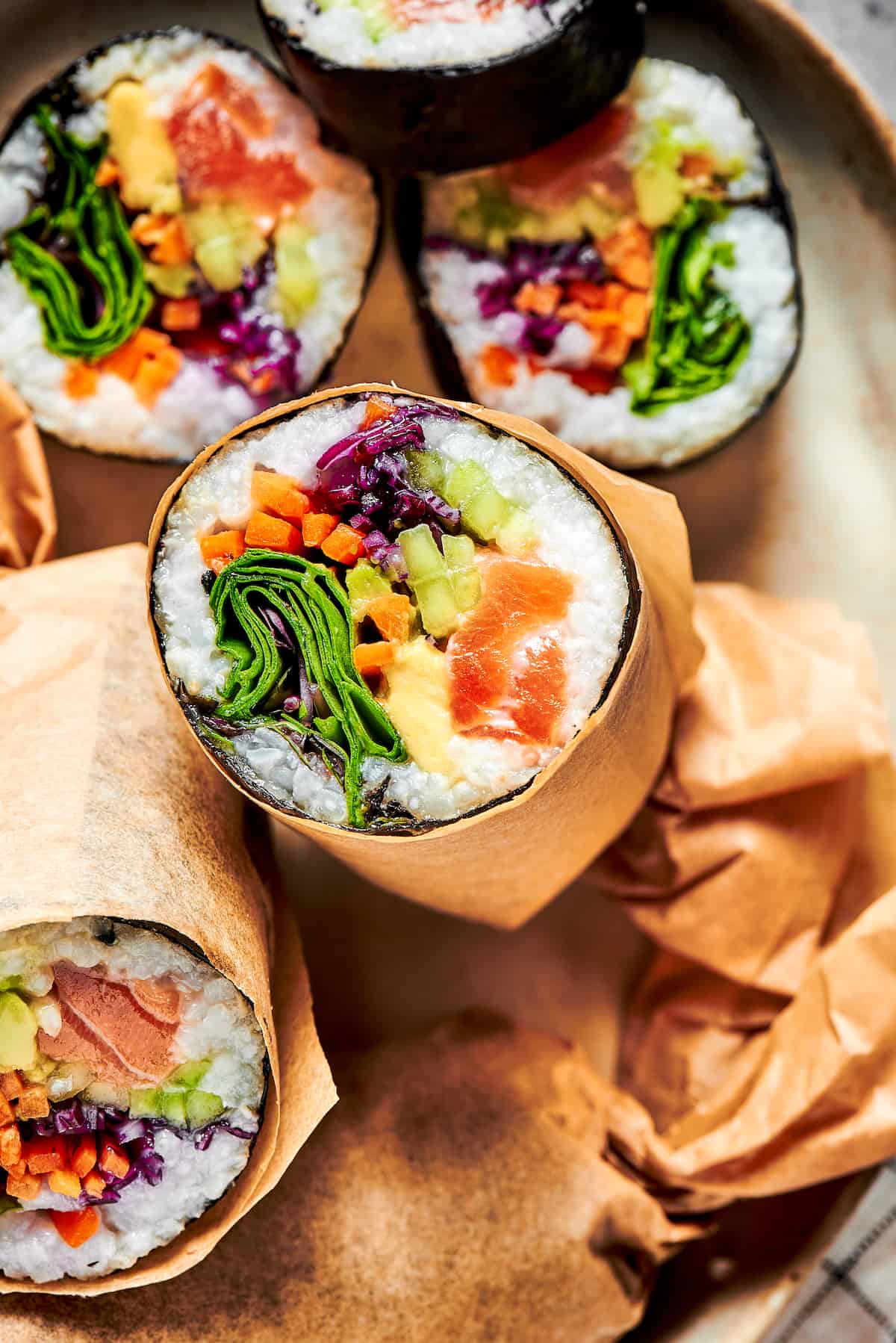 This Sushi Burrito recipe results in a giant sushi roll stuffed with spicy salmon, rice, avocado, carrots, and other veggies. Close up of a sushi burrito cut in half