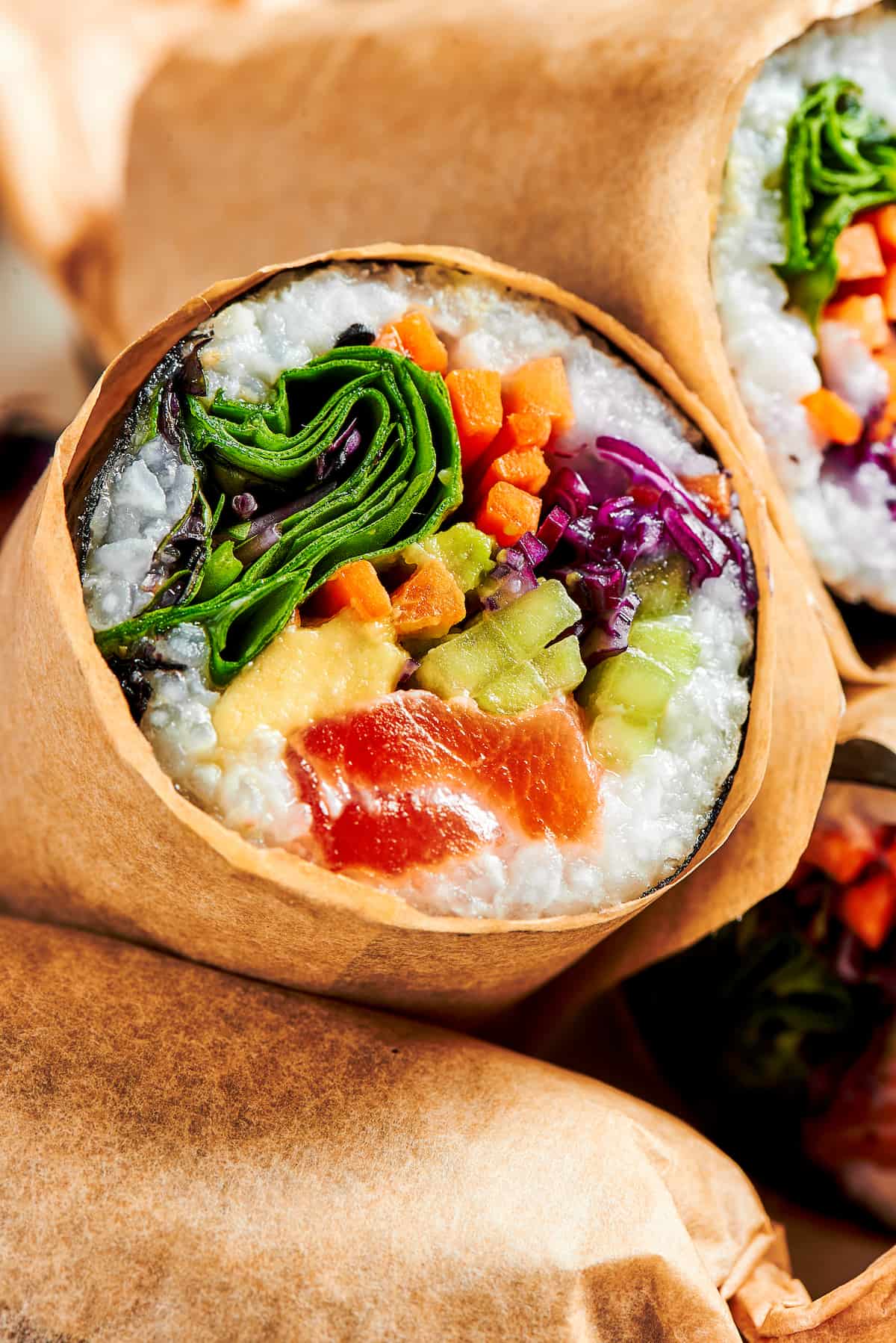 This Sushi Burrito recipe results in a giant sushi roll stuffed with spicy salmon, rice, avocado, carrots, and other veggies. Close up of half of a sushi burrito