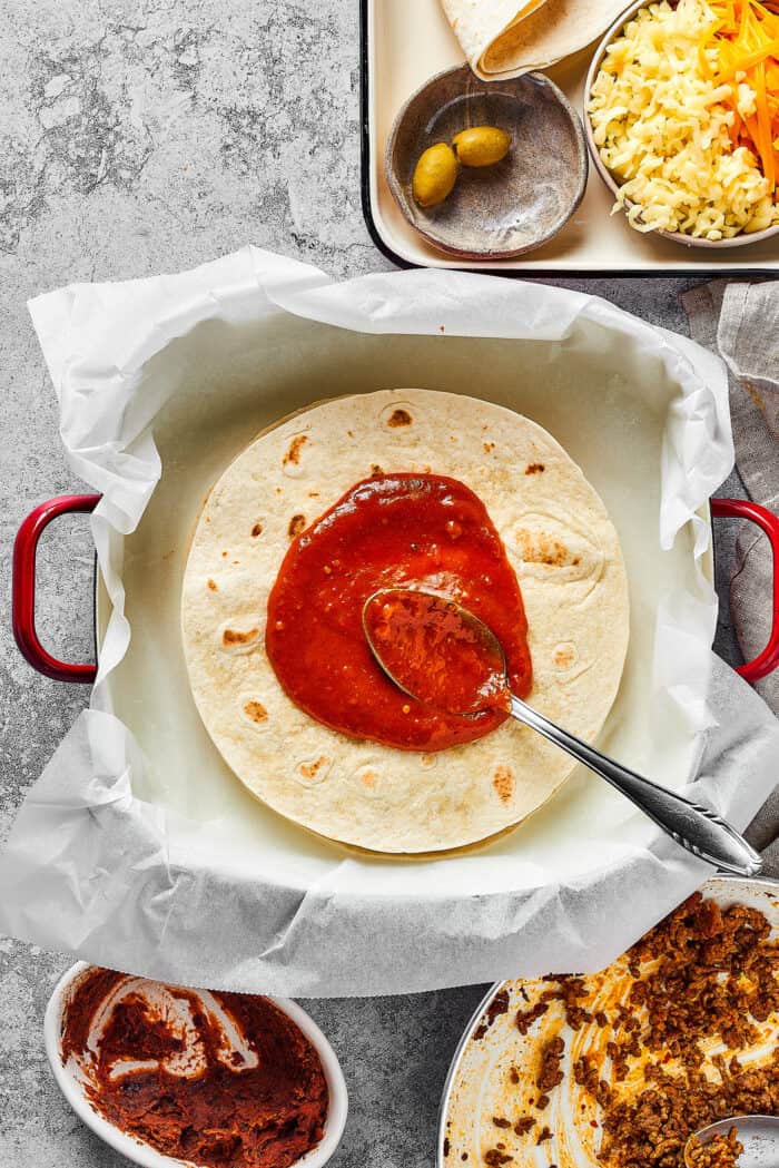 Made with taco meat, refried beans, and enchilada sauce layers with tortillas and cheese, Mexican Pizza is easy & tasty. adding enchilada sauce to the top of a tortilla