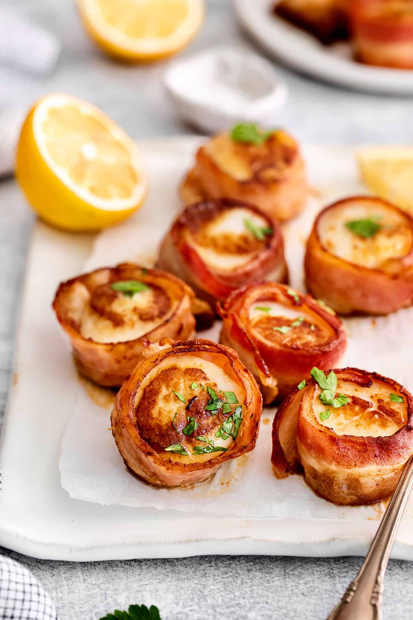 These Bacon Wrapped Scallops are tender and juicy, surrounded by crisp bacon, and topped with a delicious garlic butter. Bacon wrapped scallops on a white platter