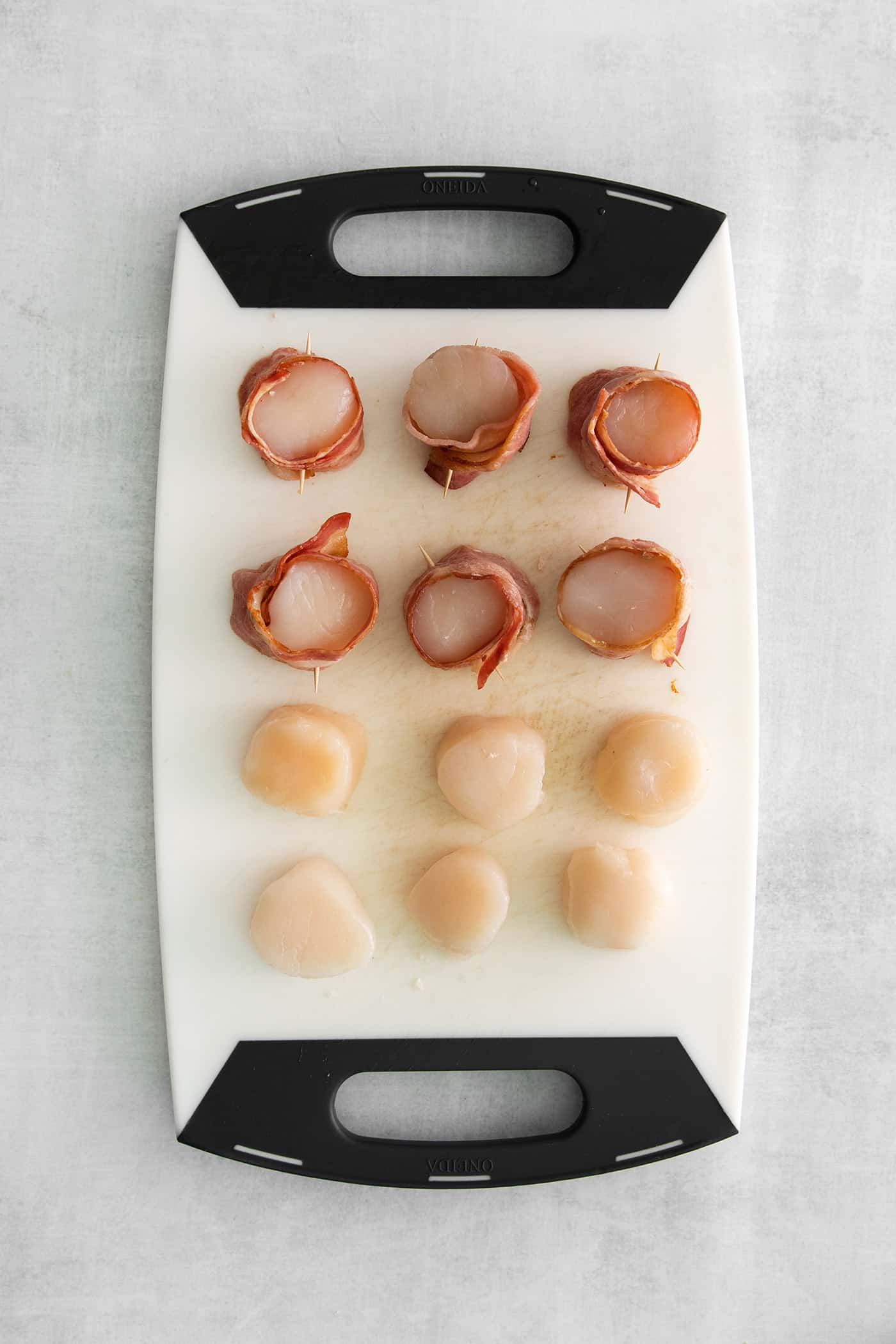 These Bacon Wrapped Scallops are tender and juicy, surrounded by crisp bacon, and topped with a delicious garlic butter. Overhead view of scallops on a cutting board