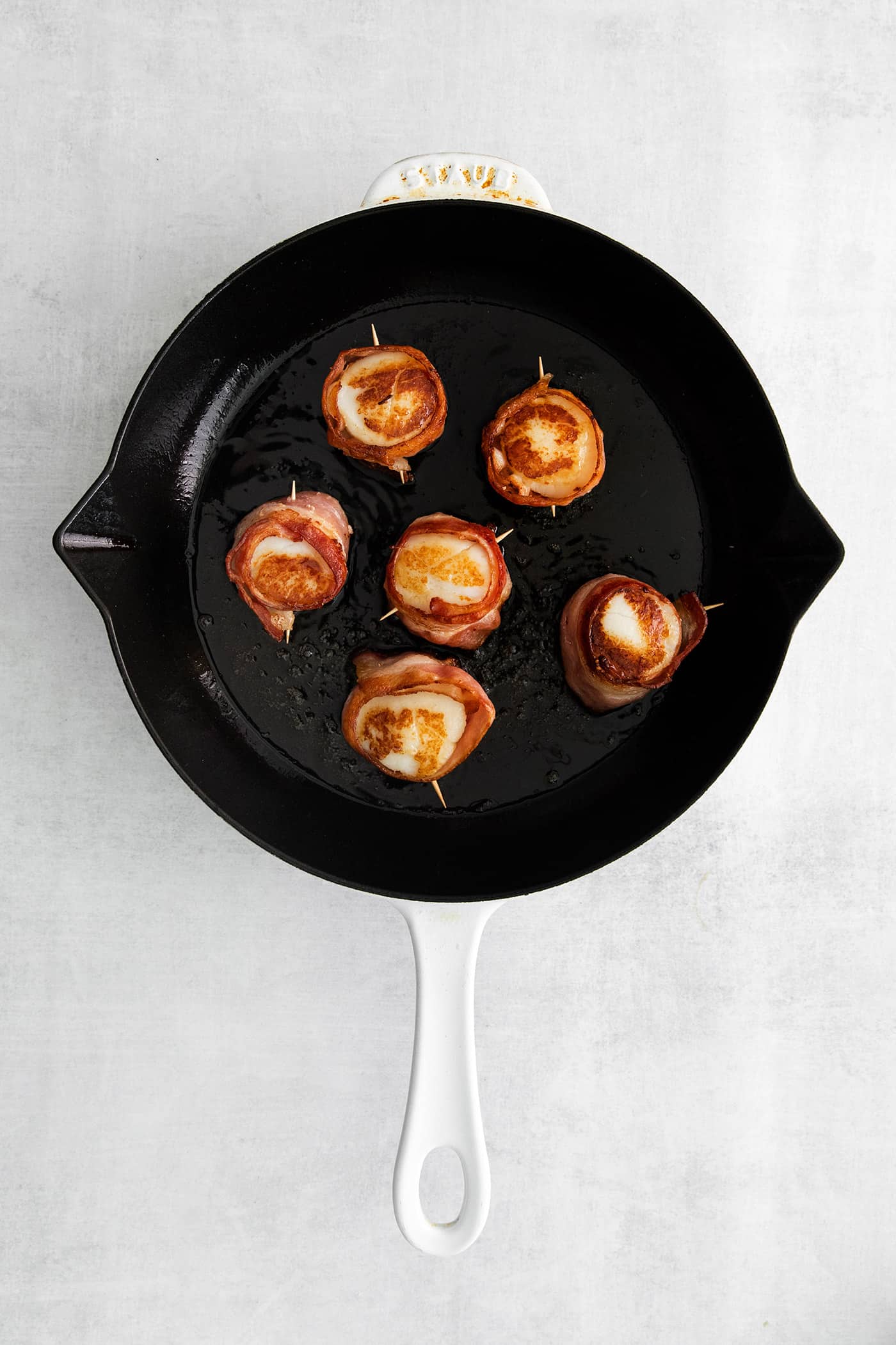 These Bacon Wrapped Scallops are tender and juicy, surrounded by crisp bacon, and topped with a delicious garlic butter. Bacon wrapped scallops in a skillet