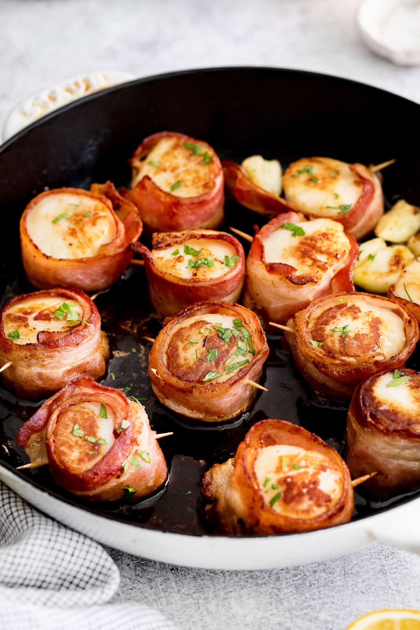 These Bacon Wrapped Scallops are tender and juicy, surrounded by crisp bacon, and topped with a delicious garlic butter. Pan seared scallops with bacon in a skillet