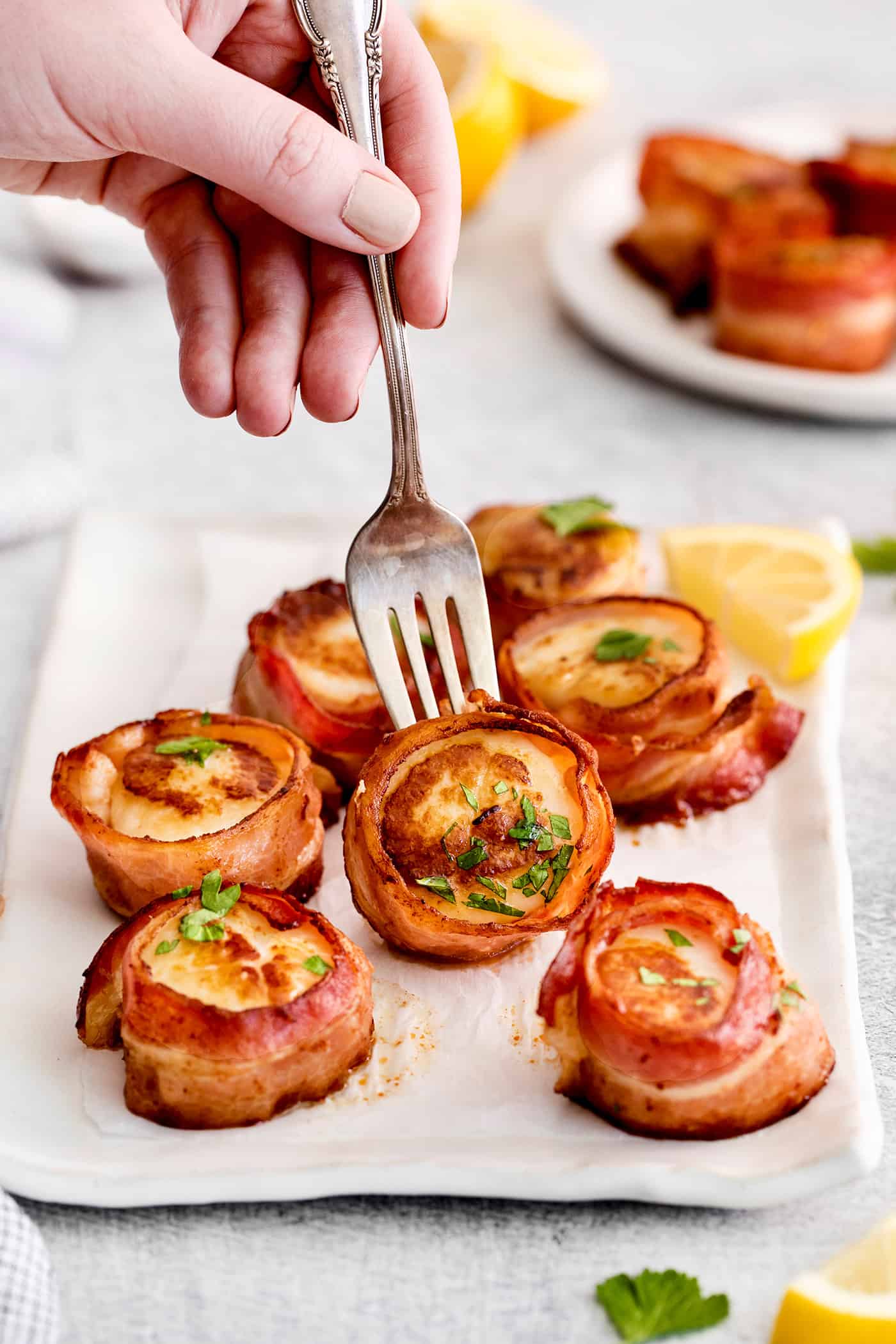 These Bacon Wrapped Scallops are tender and juicy, surrounded by crisp bacon, and topped with a delicious garlic butter. A fork grabbing a bacon wrapped scallop