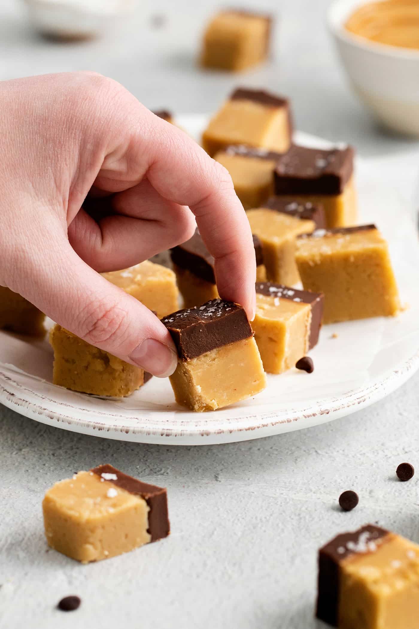 This Buckeye Fudge is a fun twist on traditional buckeyes, with smooth, creamy peanut butter fudge topped with a layer of rich chocolate. Fingers grabbing a piece of buckeye fudge
