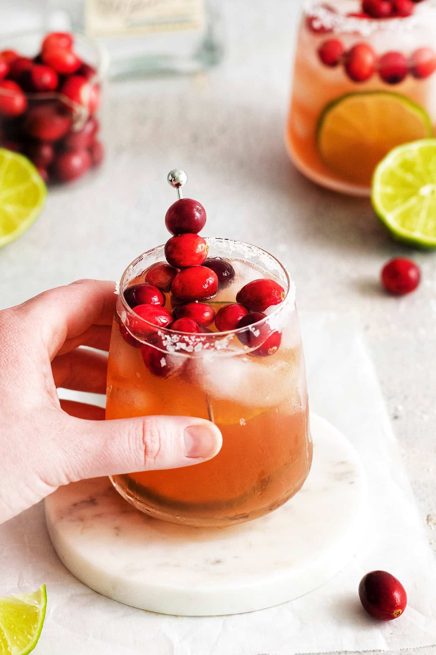 This Cranberry Margarita is tart and refreshing with flavors of cranberry and lime. A great Christmas margarita option! A hand holding a cranberry margarita