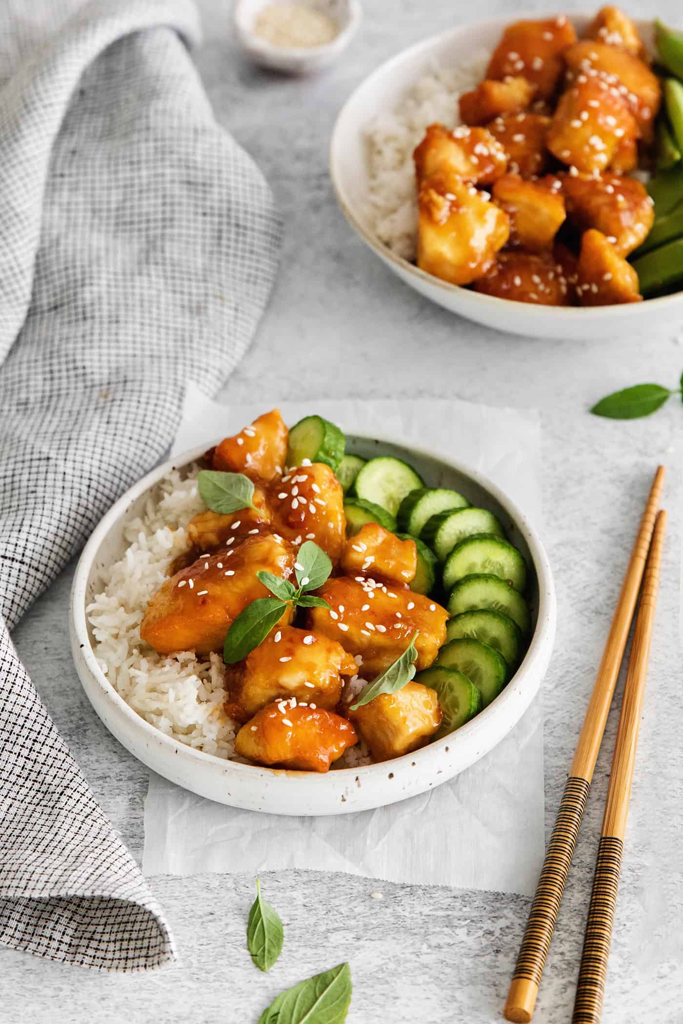 These Honey Garlic Chicken Bowls are quick and easy with moist chunks of chicken tossed in a sweet and sticky garlic sauce. A chicken rice bowl next to chopsticks