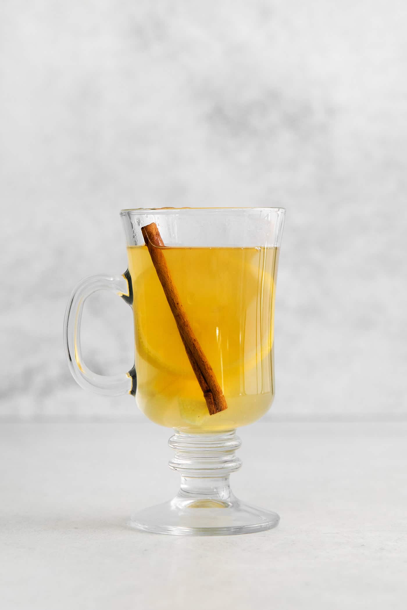 This Hot Toddy is the perfect winter drink! It’s warm and cozy with a hint of earthy honey, spicy ginger, and a burst of lemon. A hot tottie in a glass mug with a cinnamon stick