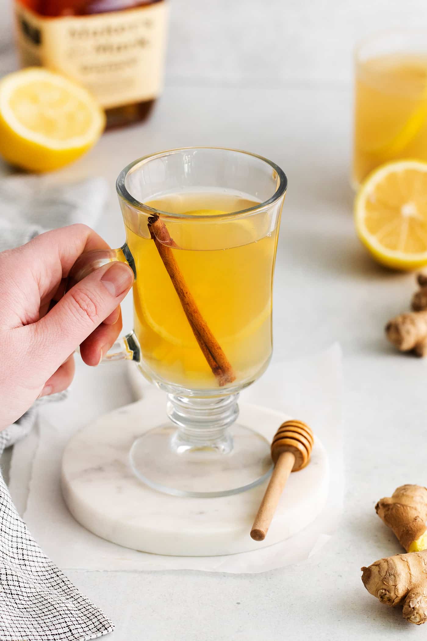 This Hot Toddy is the perfect winter drink! It’s warm and cozy with a hint of earthy honey, spicy ginger, and a burst of lemon. A hand grabbing a glass mug