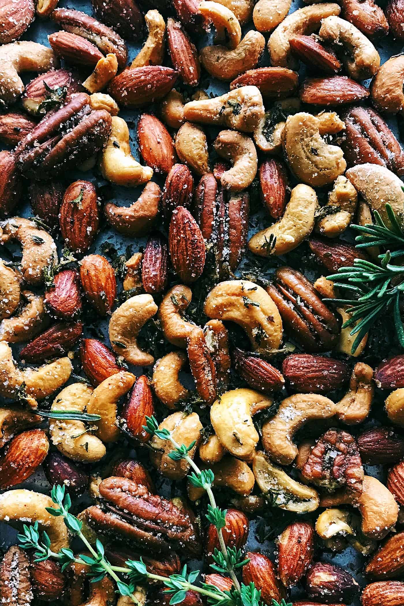 This homemade, baked spiced nuts recipe with herb-infused olive oil, cumin, spicy cayenne, and sugar is an easy holiday appetizer. Close-up of my spiced nuts recipe with fresh rosemary and thyme.