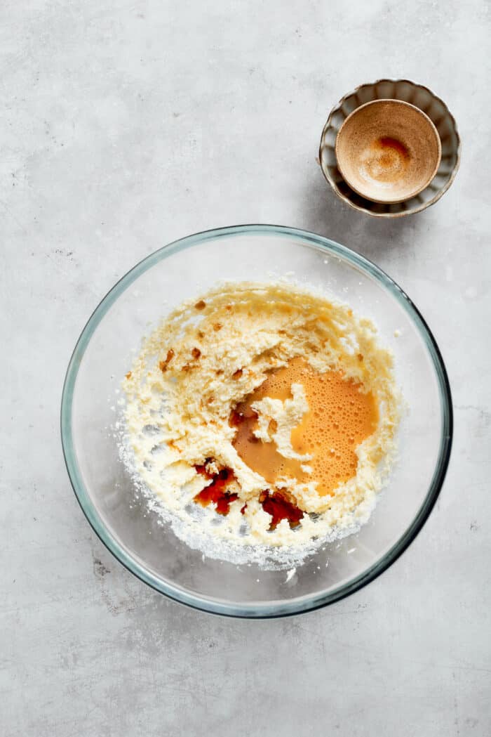 Adding eggs and vanilla to a bowl with butter and sugar.