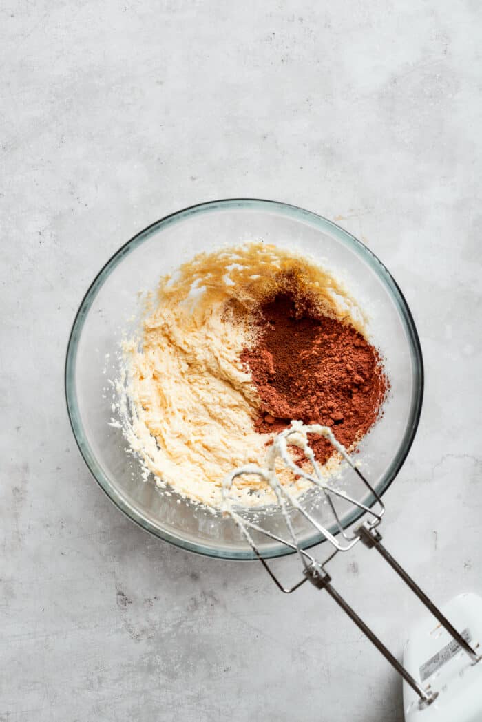Adding cocoa powder to a bowl with fluffy butter and sugar.