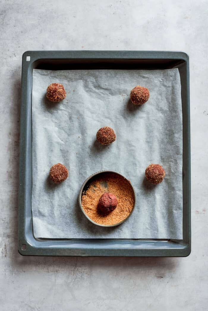 Balls of chocolate espresso cookie dough being rolled in sugar.