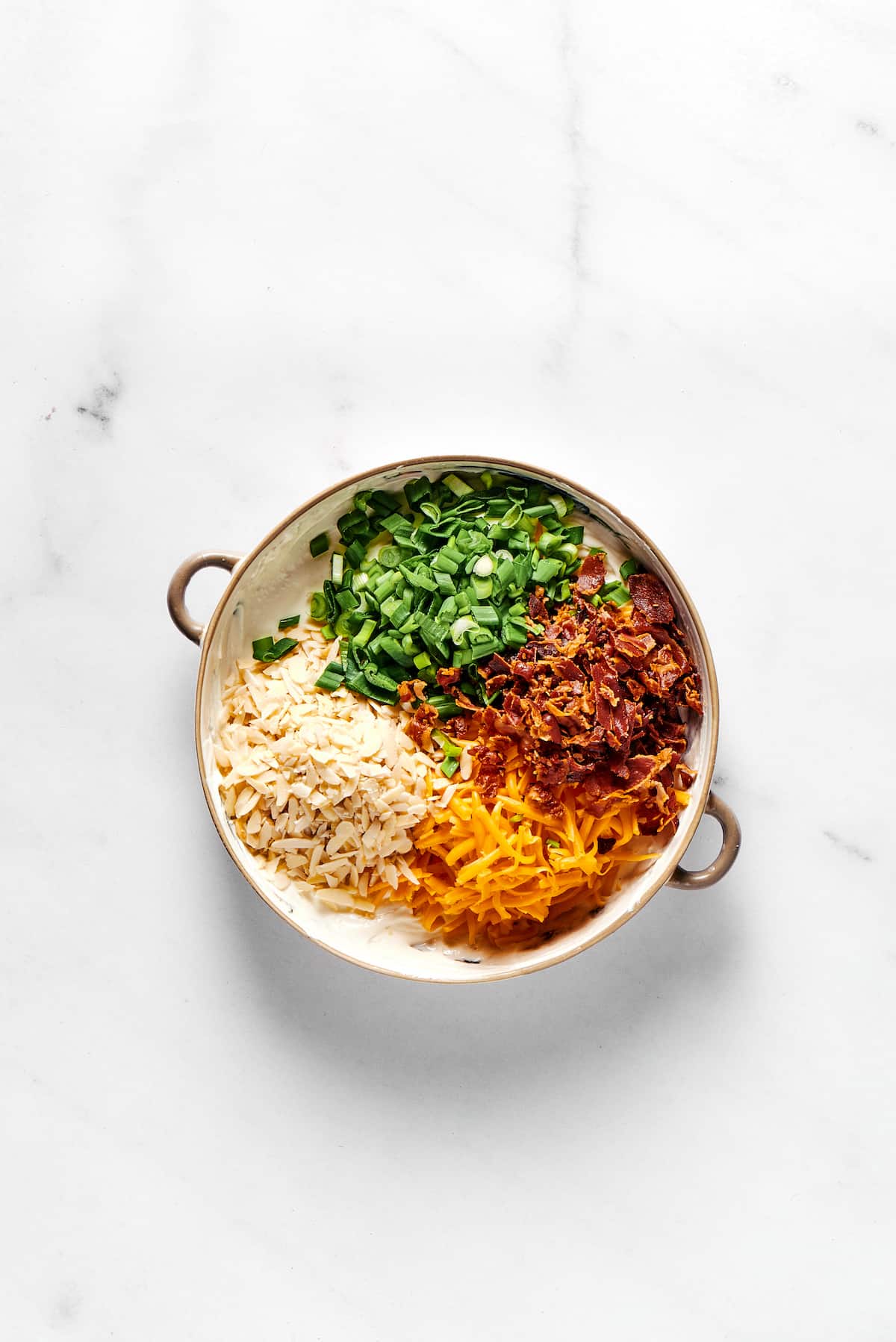 Million Dollar Dip is creamy, cheesy, and super easy to make. With cheese, bacon, and almonds, it's a super addicting party dip. Green onions, almonds, cheddar cheese, and bacon in a bowl.