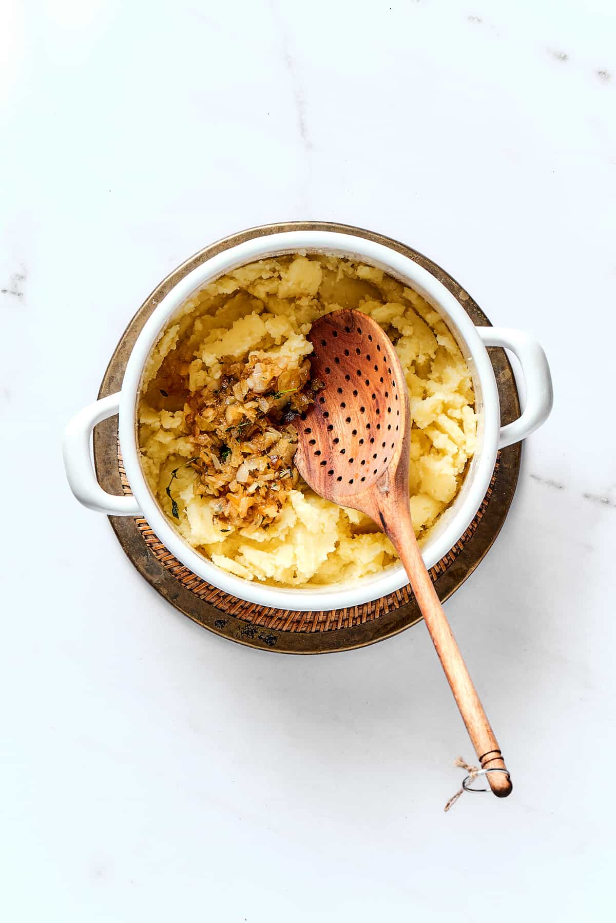Potato Knishes are a popular Jewish recipe featuring a mashed potato and onion filling wrapped in a thin, flaky dough and baked to golden. A wooden spoon mashing potatoes