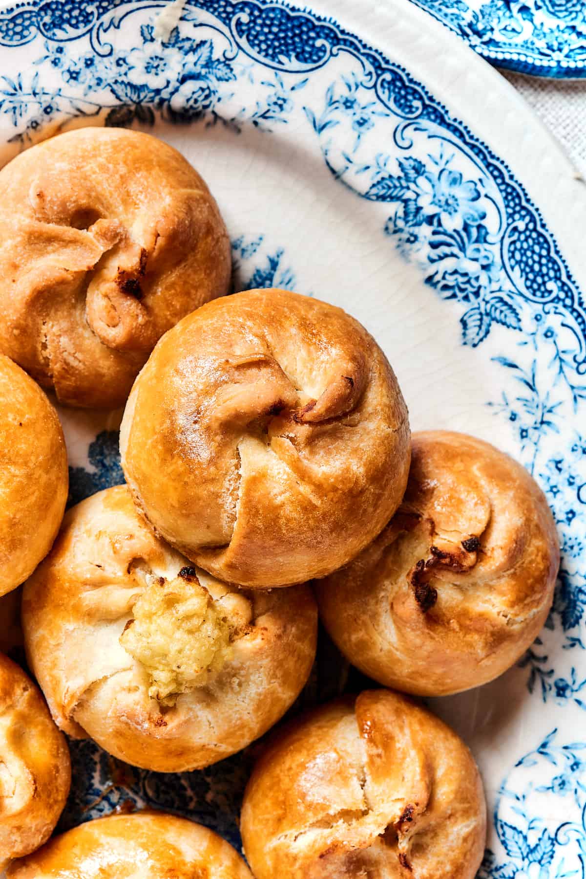 Potato Knishes are a popular Jewish recipe featuring a mashed potato and onion filling wrapped in a thin, flaky dough and baked to golden. Close up of a plate of potato knishes