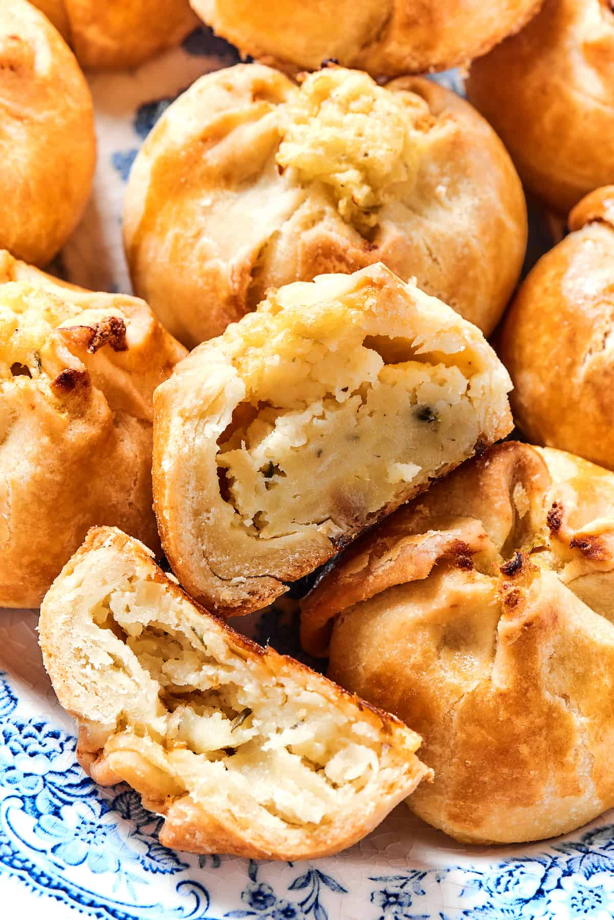 Potato Knishes are a popular Jewish recipe featuring a mashed potato and onion filling wrapped in a thin, flaky dough and baked to golden. Close up of potato knishes, with one cut in half