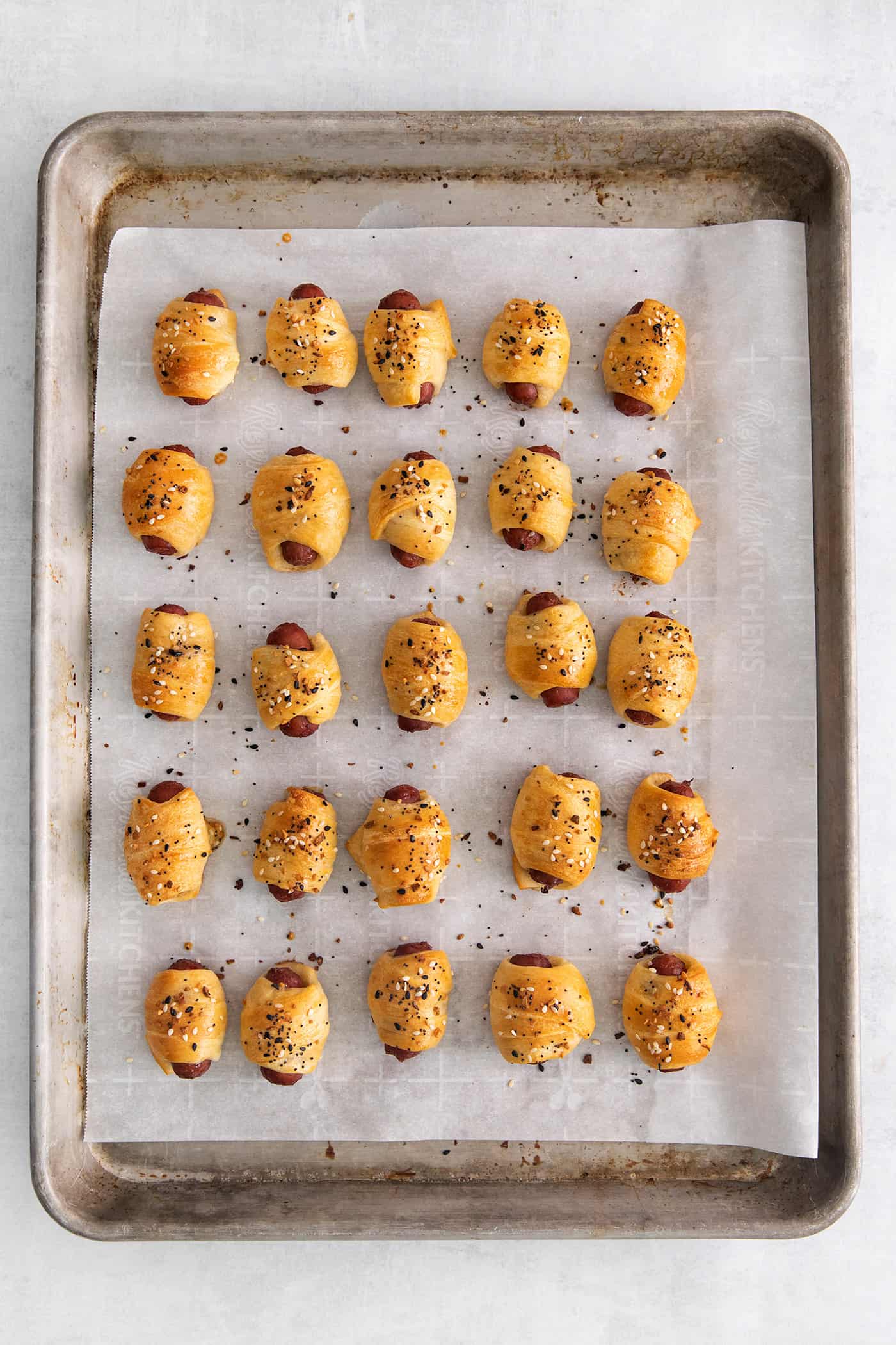 Everything Bagel Pigs in a Blanket are the perfect appetizer– mini sausage wrapped in crescent dough, topped with everything bagel seasoning Mini pigs in a blanket on a baking sheet