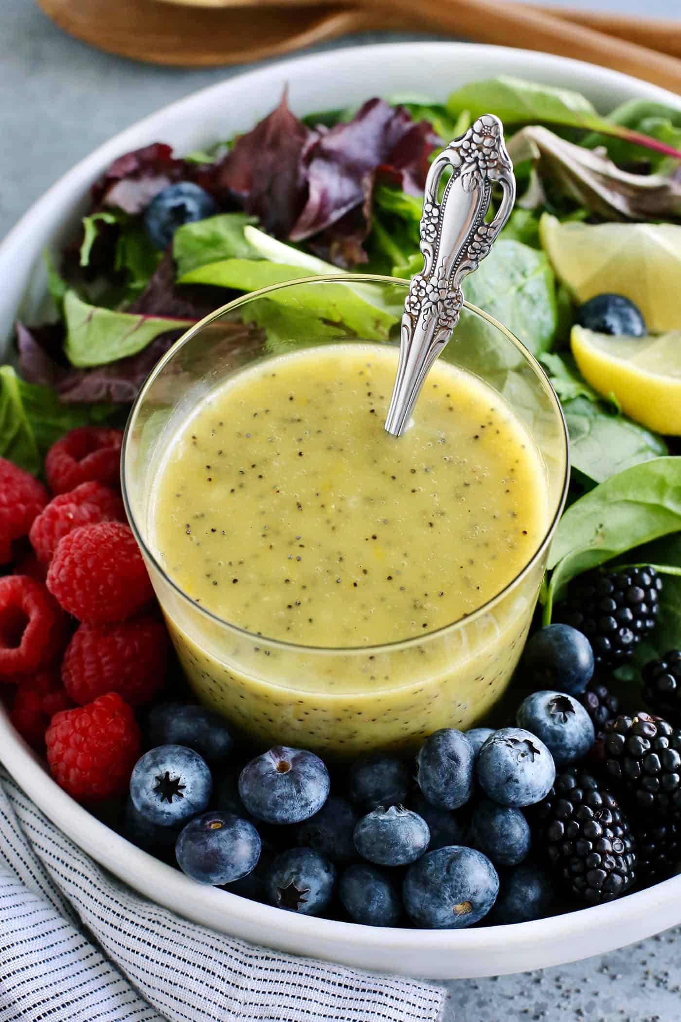 A quick & easy homemade poppy seed dressing with bright lemon flavor and a light, creamy consistency. It's versatile, fresh, and delicious! a cup of lemon poppy seed dressing and a bowl of fresh greens and berries