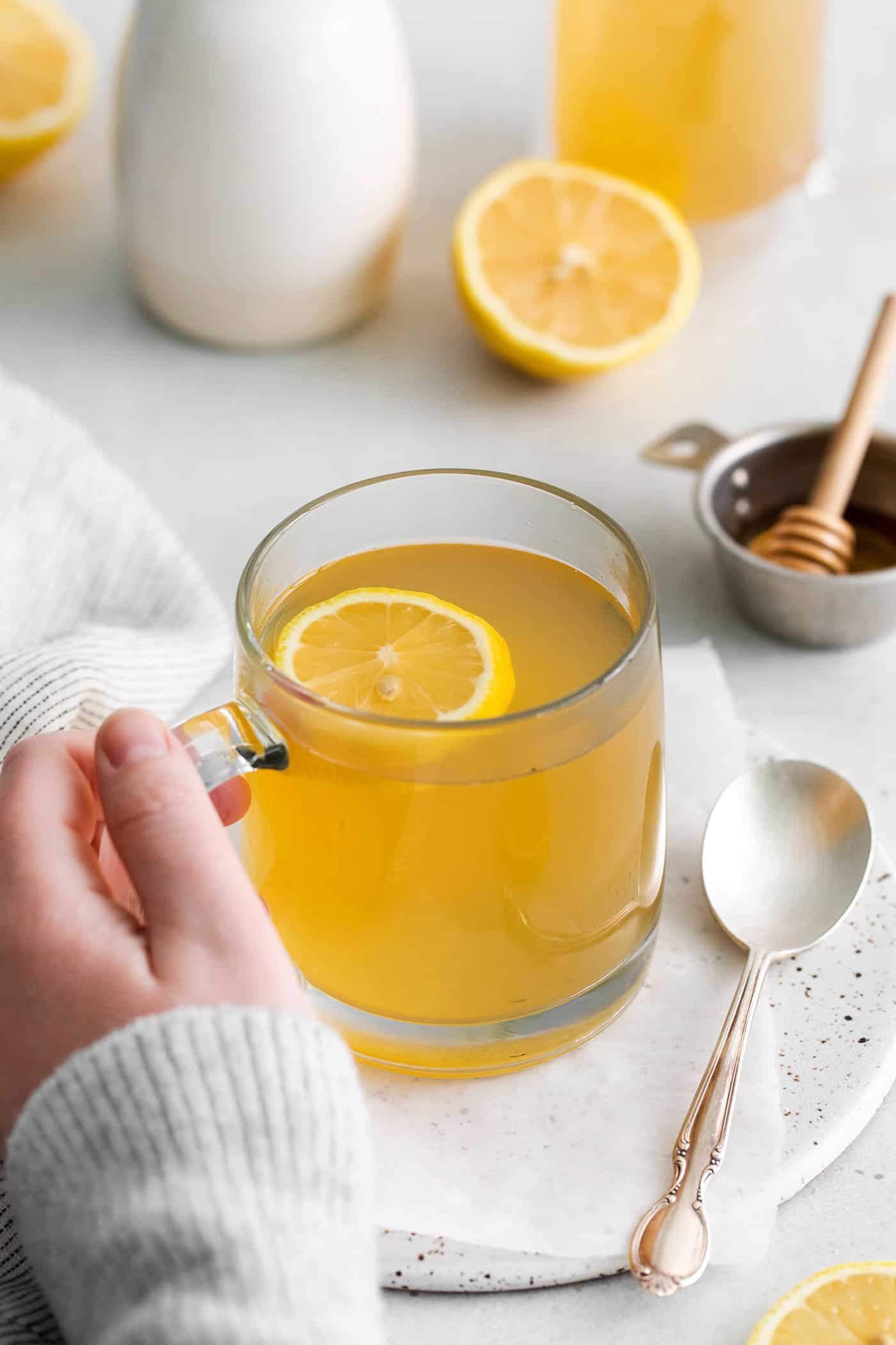Made with citrus mint and peach tea, lemon, and honey, Starbucks Medicine Ball Recipe is just the thing for those chilly months. A hand holding a mug of medicine ball tea with lemon slices