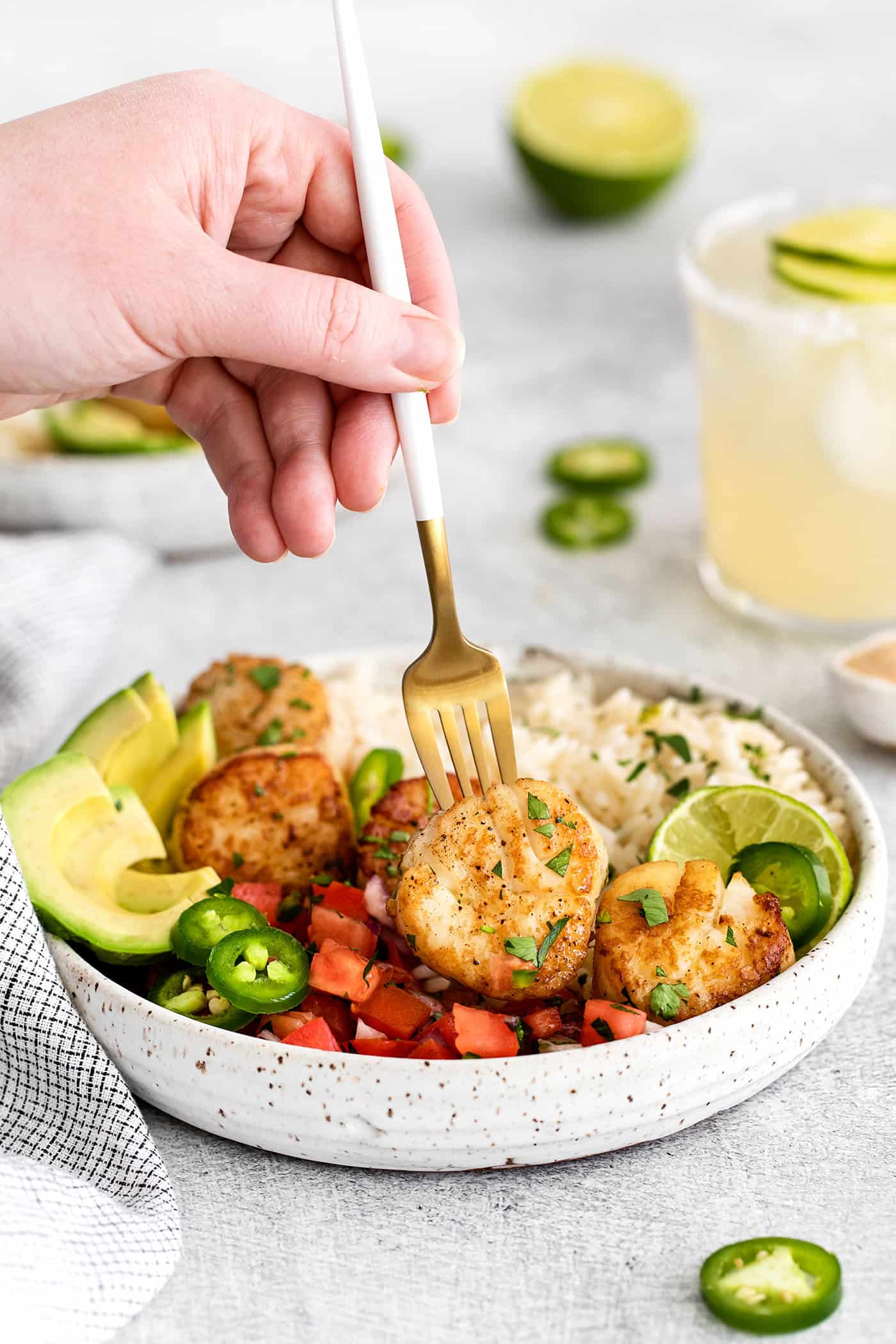 These Tex-Mex Scallop Rice Bowls are bright, refreshing, and packed with flavor, with scallops, pico de gallo, and lime crema. A fork spearing a scallop in a rice bowl