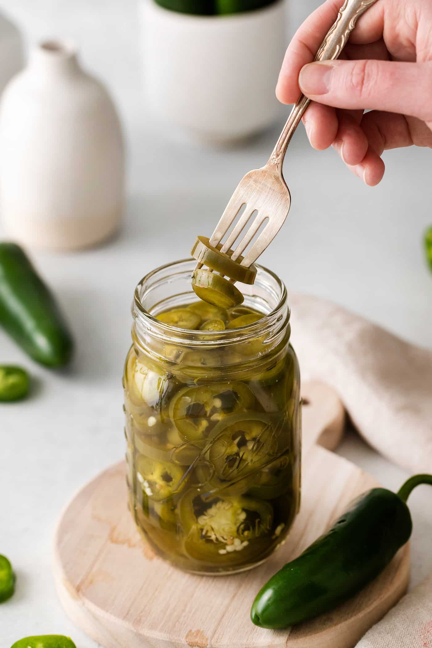 With just 5 ingredients, these Pickled Jalapenos are spicy and tangy. Add them to sandwiches and salads or straight from the jar. A fork pulling a jalapeno slice from a jar