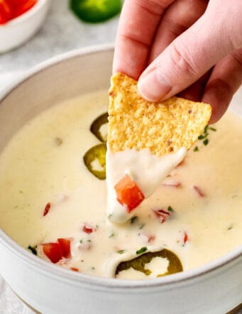 A hand dipping a tortilla chip into queso blanco