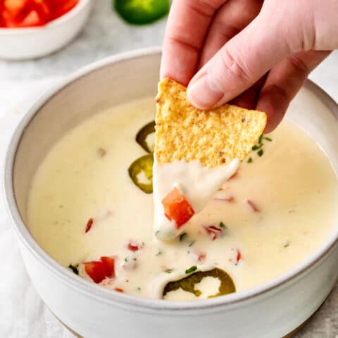 A hand dipping a tortilla chip into queso blanco