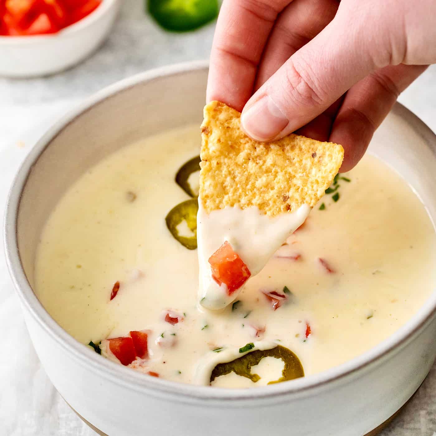A hand dipping a tortilla chip into queso blanco