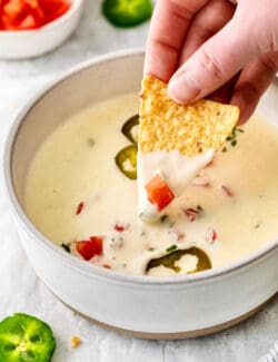A hand dipping a tortilla into queso blanco