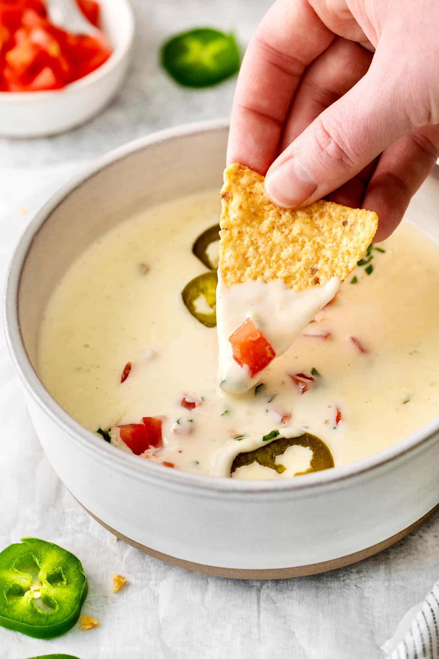 Smooth and creamy with just the right amount of heat, this Homemade Queso Blanco is made with just 5 ingredients! Quick & easy! A hand dipping a tortilla into queso blanco
