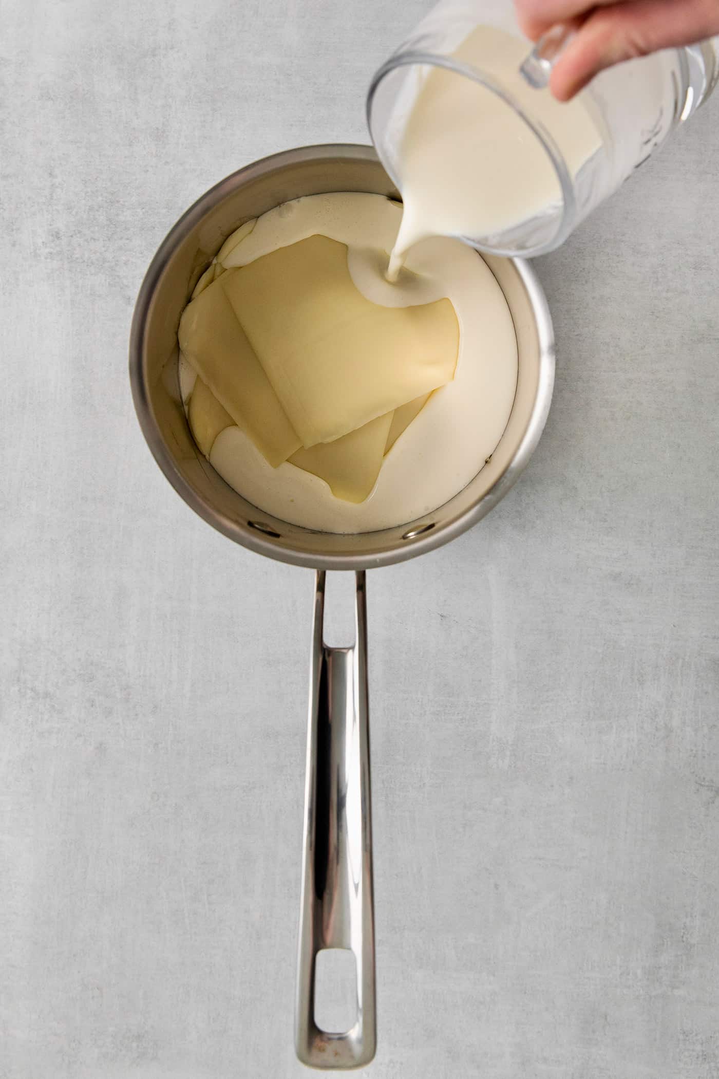 Smooth and creamy with just the right amount of heat, this Homemade Queso Blanco is made with just 5 ingredients! Quick & easy! Heavy cream being poured over slices of American cheese in a saucepan