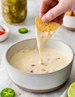 A hand dipping a tortilla into queso blanco